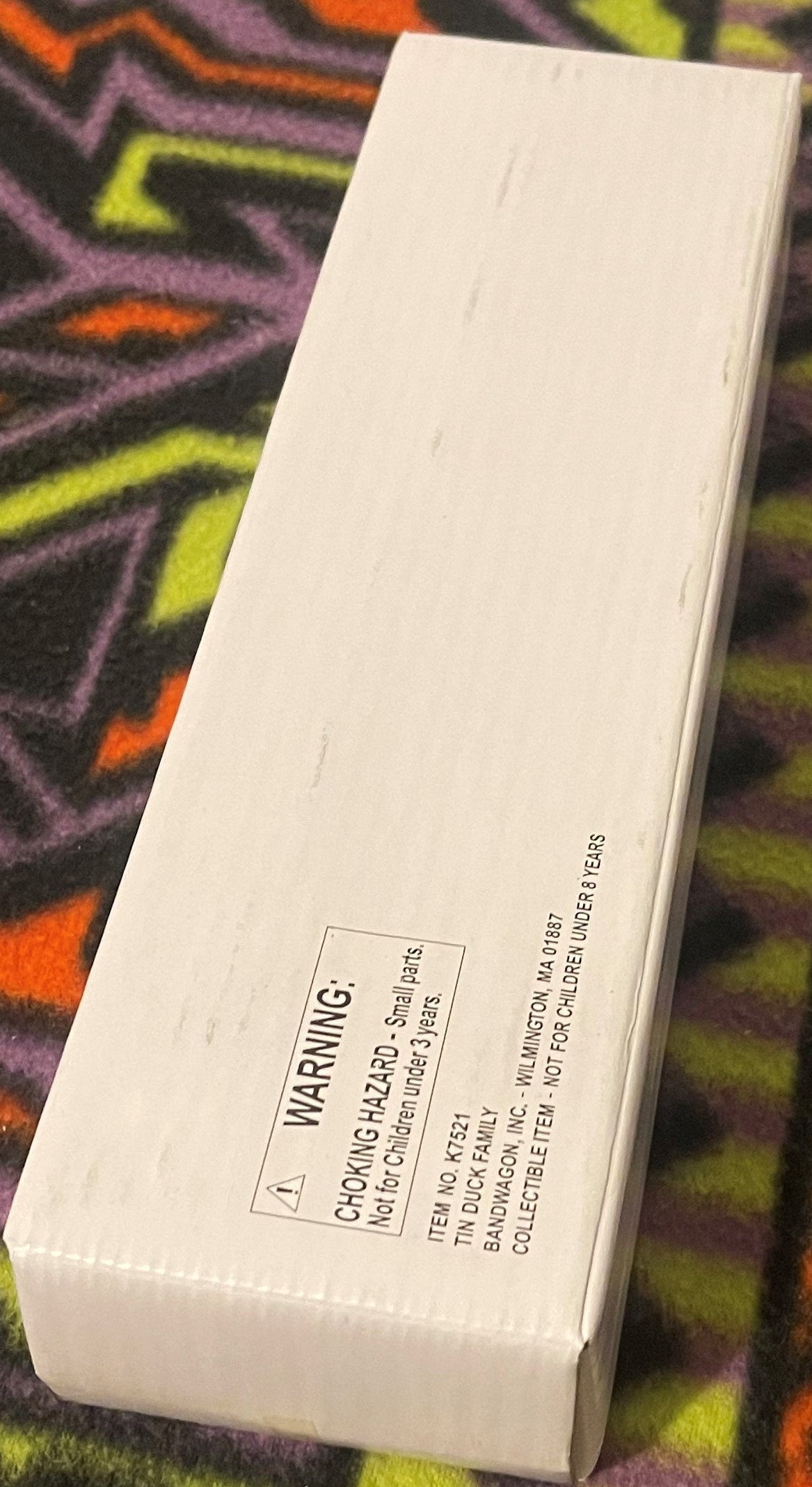 The white Bandwagon box photographed at an angle on patterned fabric, its printed warning and item panel running along the side.
