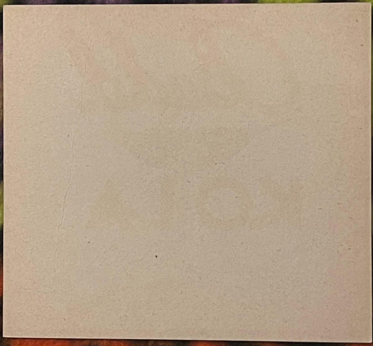 Blank cream-colored cardstock or label with visible texture and minor marks, displayed against dark border