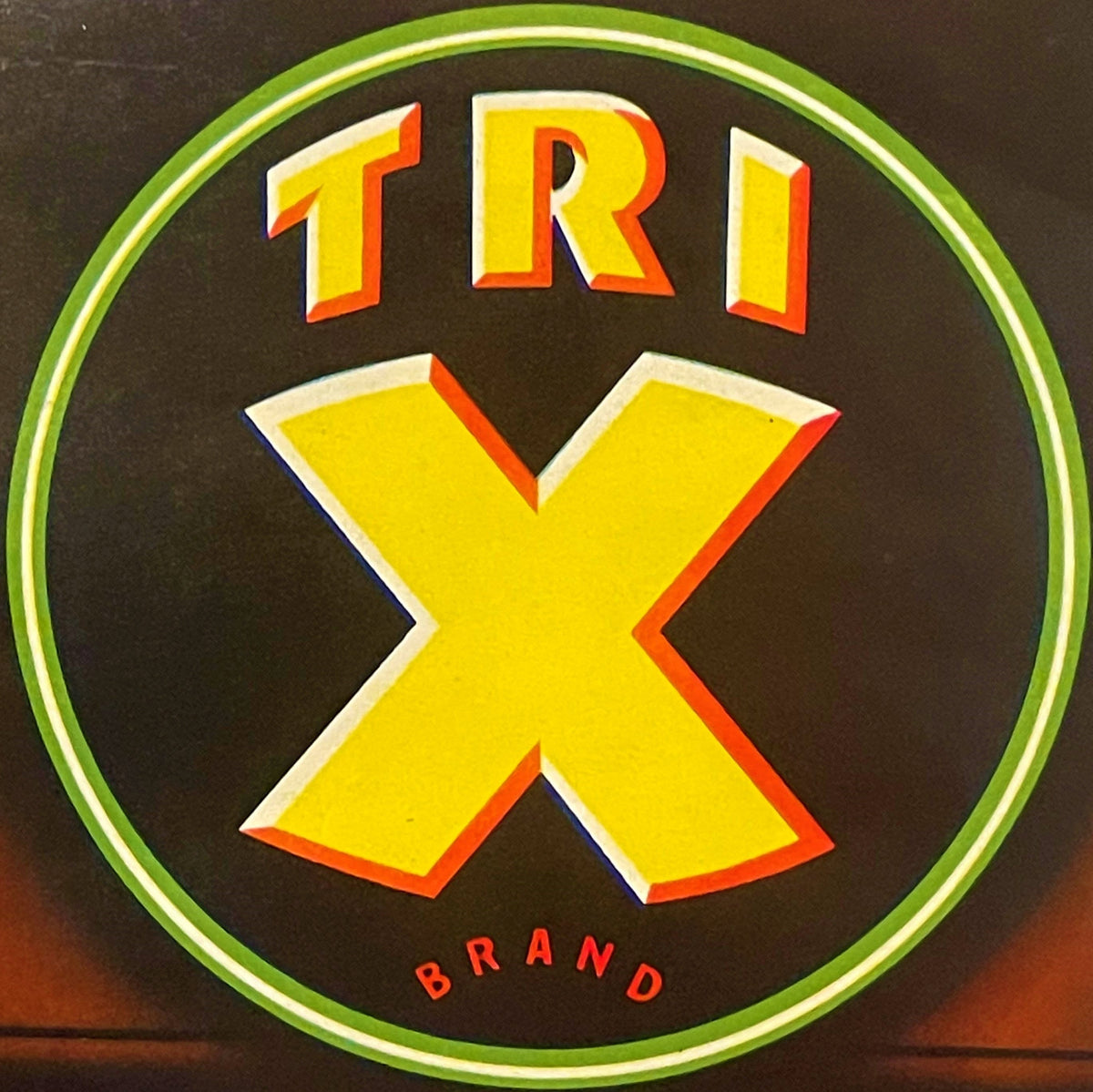 Vintage circular crate label with yellow "TRI" text and large X symbol, green border, dark background, "BRAND" text at bottom