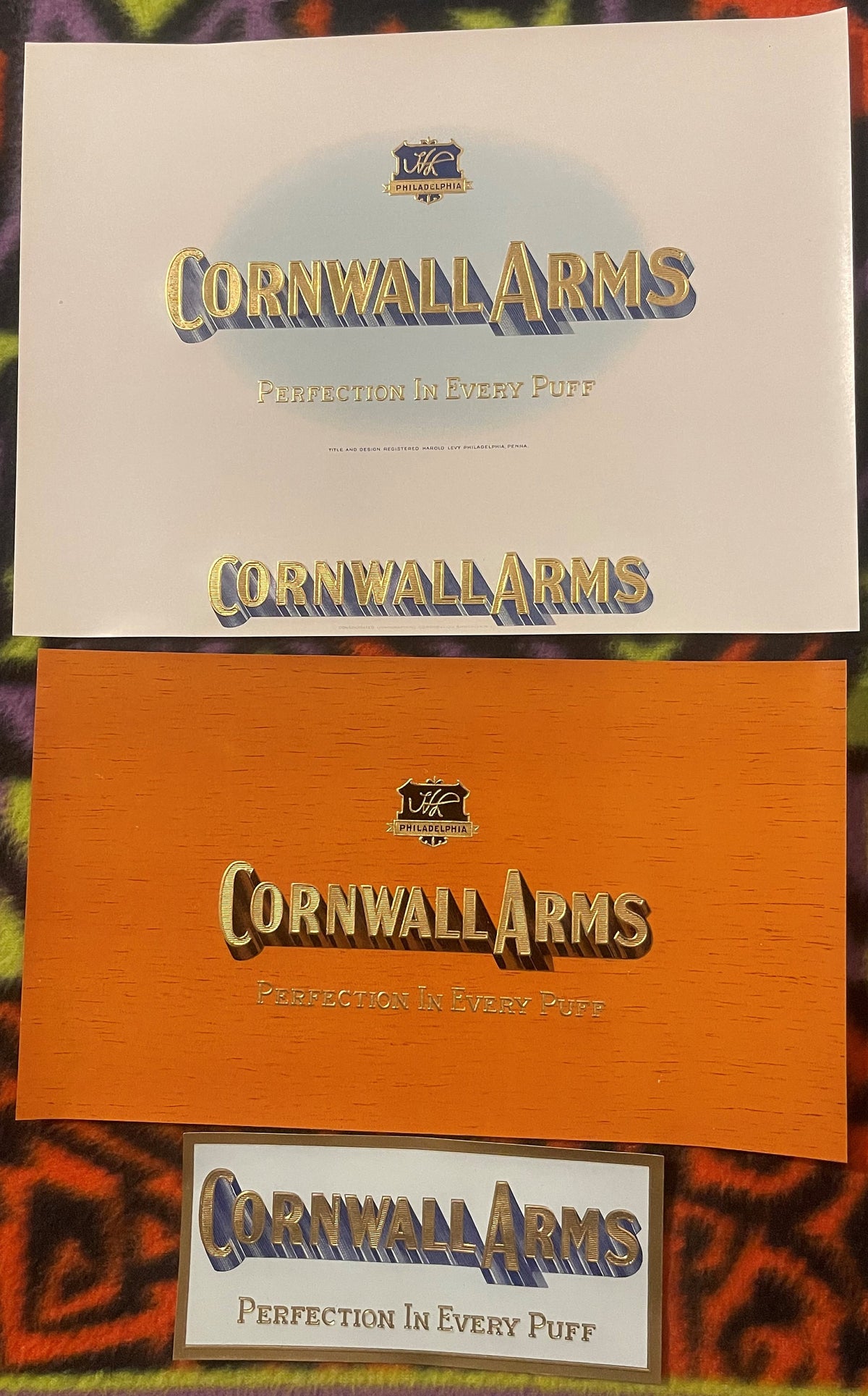 Three Cornwall Arms cigar labels stacked: a cream sheet, an orange wood-grain sheet, and a small label, each with gold-embossed lettering and the HL Philadelphia shield