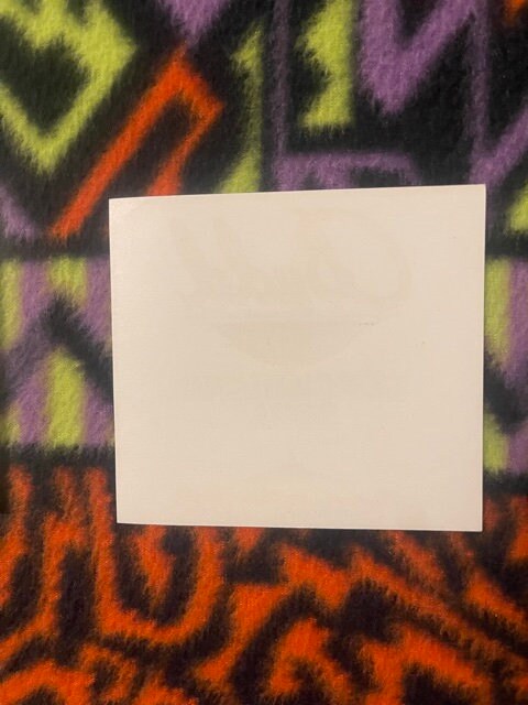Blank cream-colored card centered on colorful geometric patterned fabric with yellow, purple, and orange zigzag designs