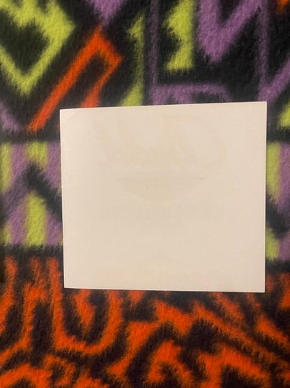 Blank cream-colored card centered on colorful geometric patterned fabric with yellow, purple, and orange zigzag designs