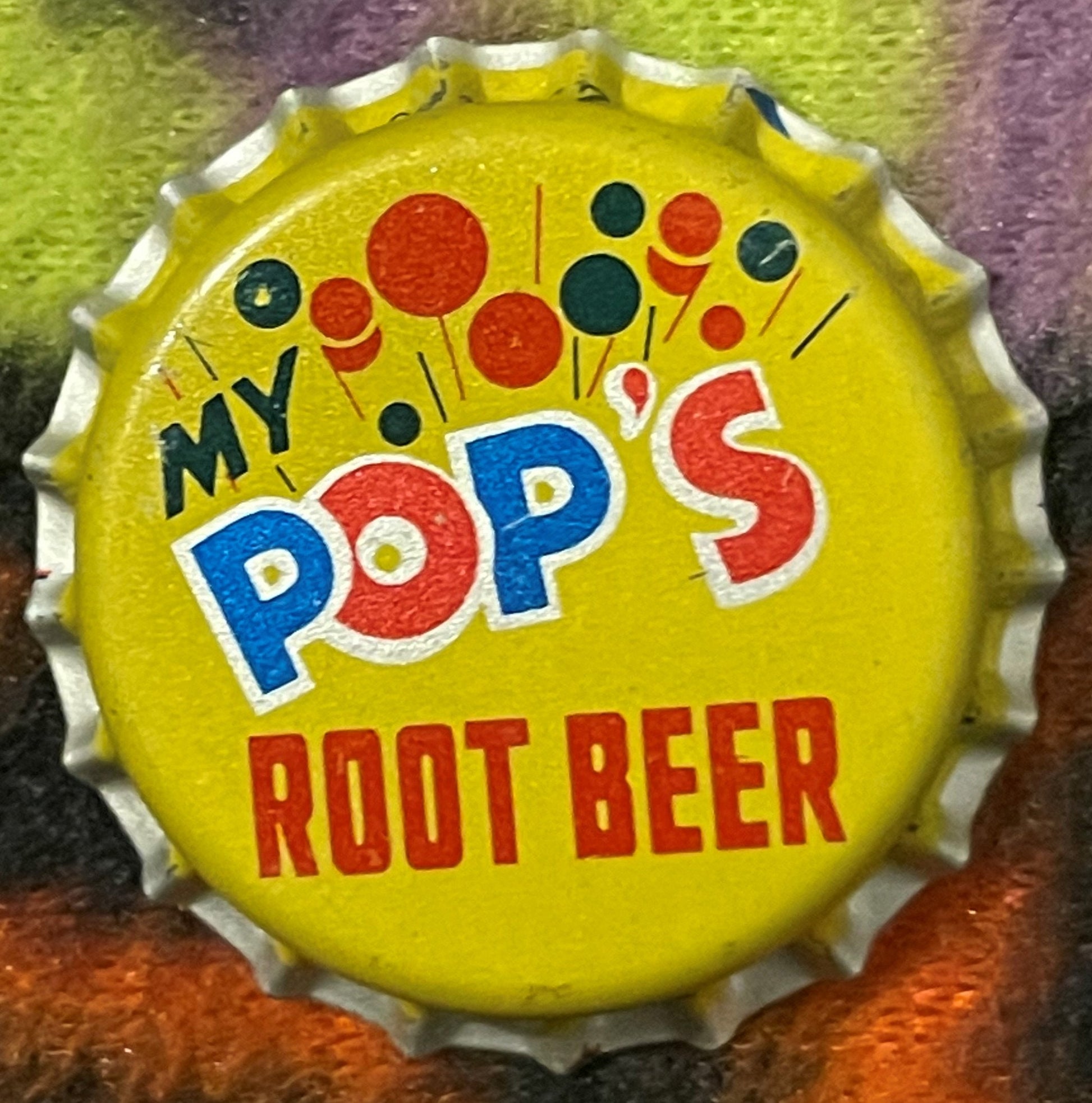 Vintage yellow bottle cap with "My Pop's Root Beer" text in blue and red lettering, decorated with red and dark blue circles,
