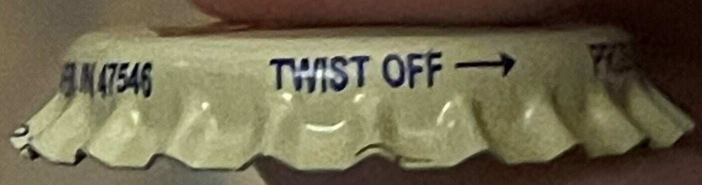 Vintage cream soda bottle cap showing "TWIST OFF" text and product code, scalloped metal edges on cream-colored background