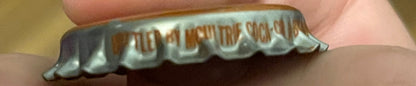 Vintage bottle cap held in hand showing embossed ridged metal edge and text, close-up side view for detail