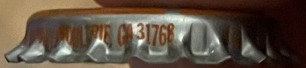 Vintage corrugated bottle cap showing embossed text and numerals, photographed from above on brown surface