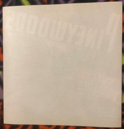 Cream-colored vintage crate label with faint embossed text reading "Pineywoods" at top, displayed against colorful patterned 