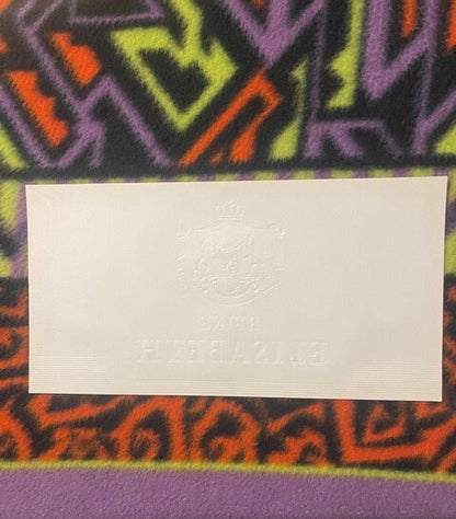 Cream-colored embossed cigar label on colorful geometric patterned fabric background for scale