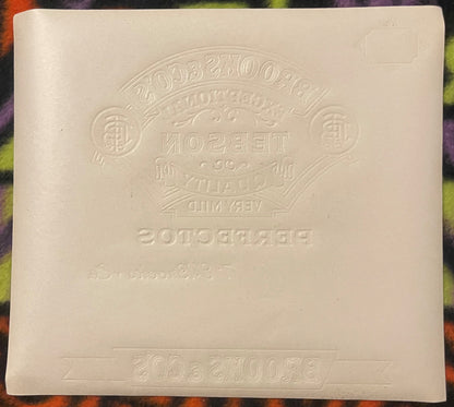 Cream-colored embossed cigar label showing "Tebson" brand text and decorative elements, photographed flat against colorful pa