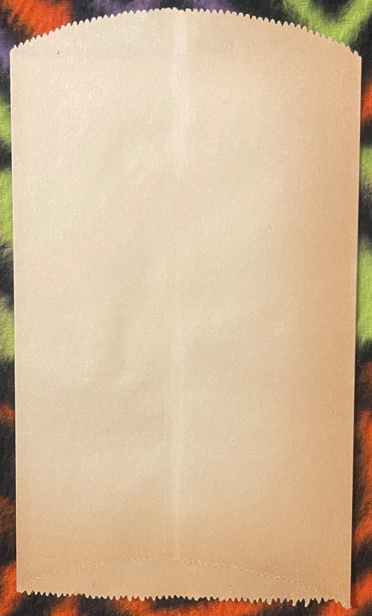 Cream-colored paper sleeve with scalloped edges displayed flat against a colorful patterned background