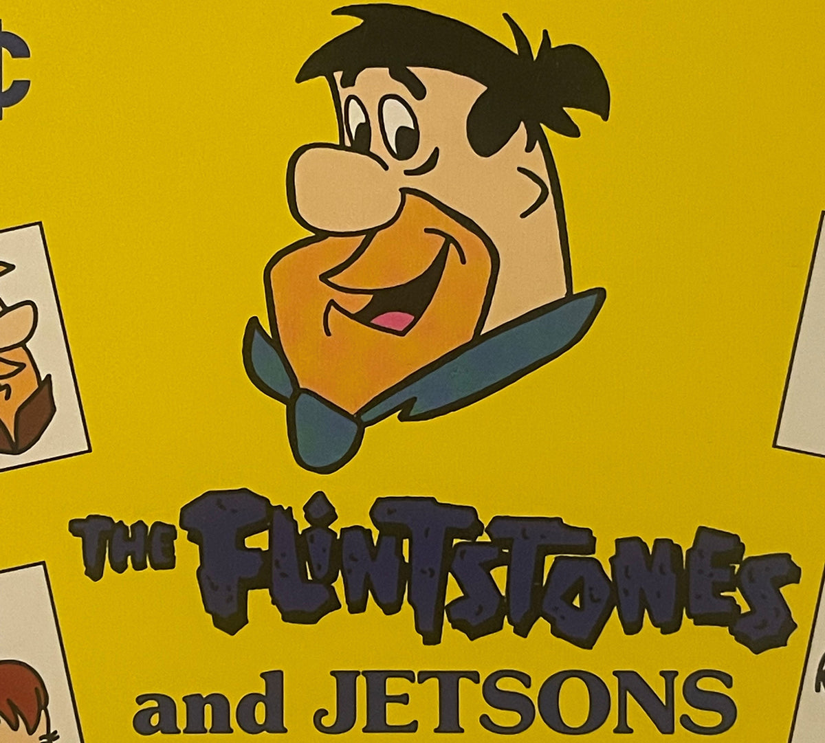 Vintage yellow vending display sign featuring Fred Flintstone character above "The Flintstones and Jetsons" text in black