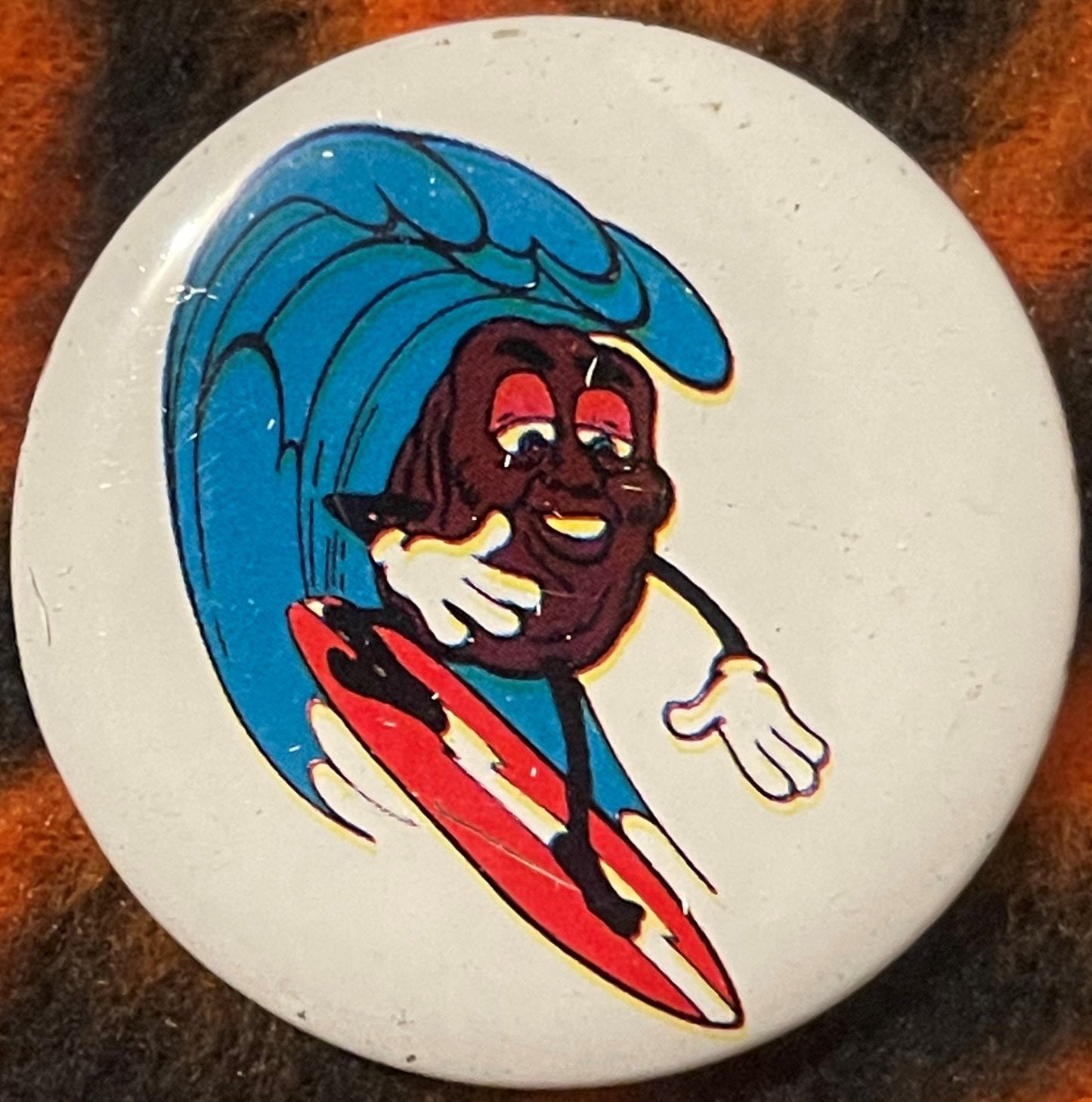 Round white pinback button featuring a cartoon character surfing on a blue wave, wearing red and yellow striped shorts, with 