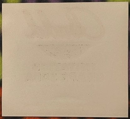 Faded cream-colored label with barely legible embossed or printed text, shown against green and red border matting