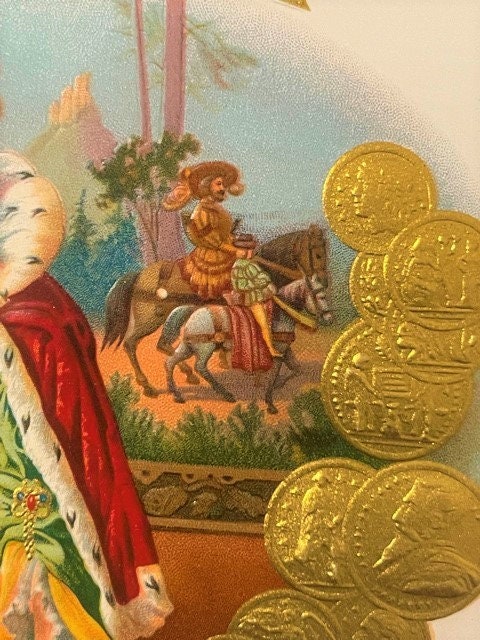 Antique gold-embossed cigar label with Victorian royalty scene, shown next to coins for scale