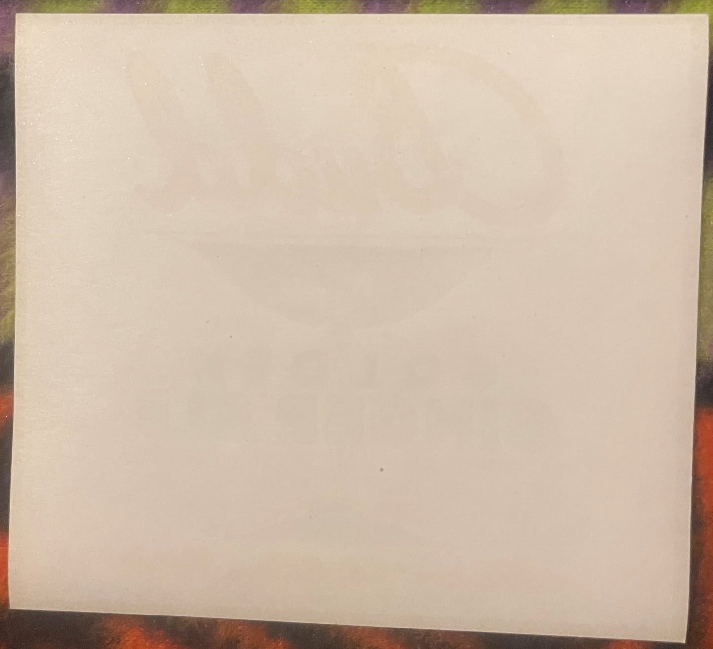 Blank cream-colored vintage label on textured wood surface with colorful background visible at edges