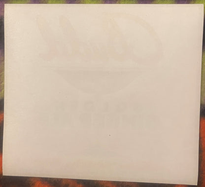 Blank cream-colored vintage label on textured wood surface with colorful background visible at edges