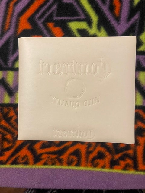 Cream-colored embossed cigar label with gold seal design on colorful patterned fabric background