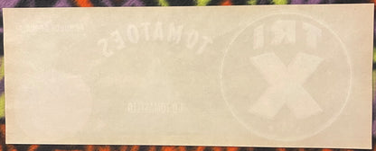 Cream-colored vintage crate label with faint embossed tomato imagery and text, displayed against a colorful patterned backgro