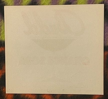 Cream-colored vintage beverage label on colorful patterned background, mostly blank with faint text