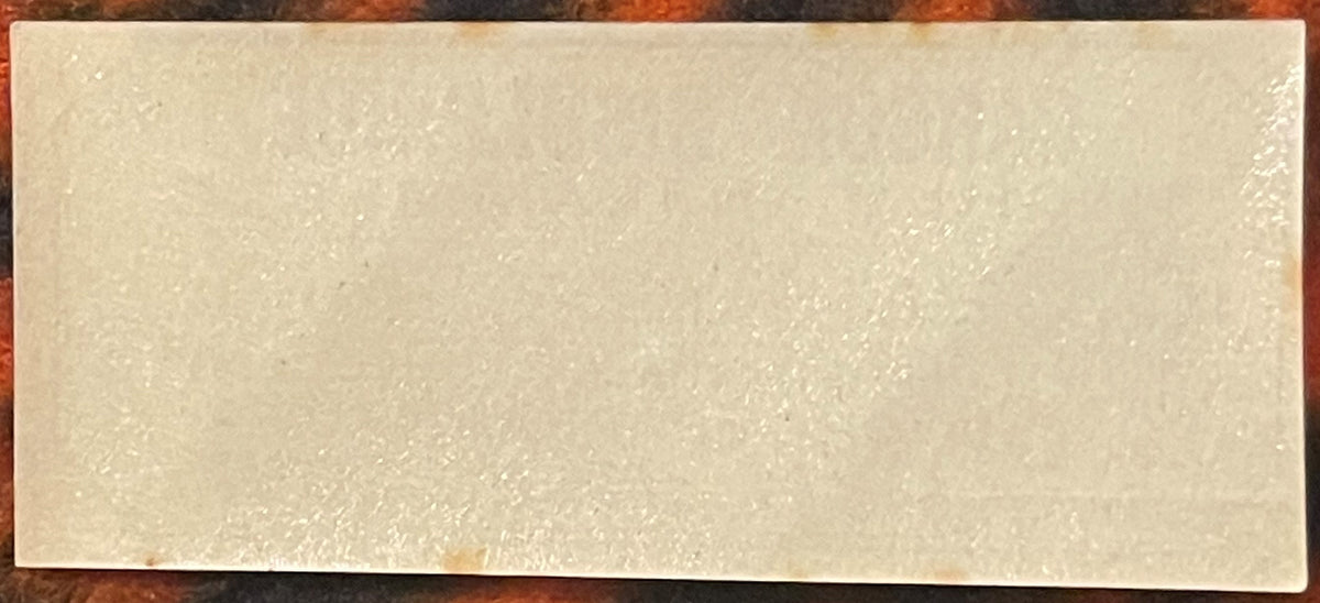 Cream-colored rectangular label with embossed or printed texture, photographed against a brick surface background