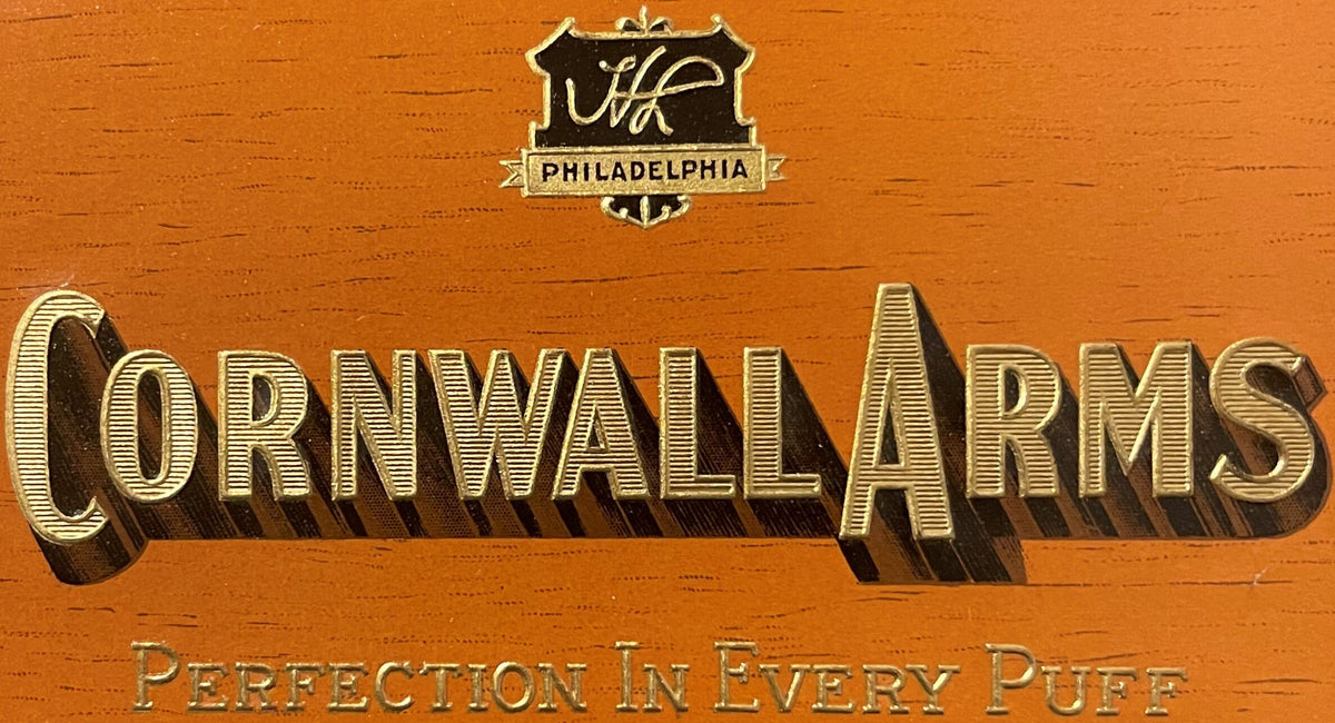 Close-up of the woodgrain Cornwall Arms label: Harold Levy's HL monogram shield over PHILADELPHIA and CORNWALL ARMS in embossed gold with a deep shadow.