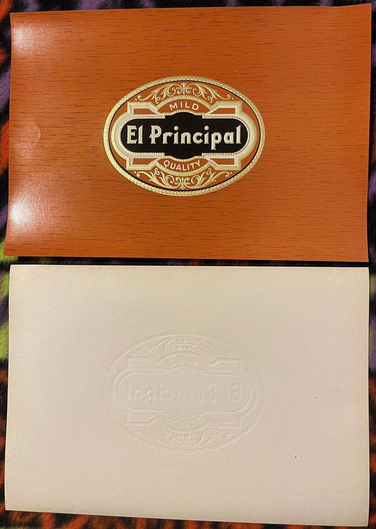 Two cigar box lids displayed: orange wood box with gold-embossed "El Principal" label marked "Mild Quality," and cream
