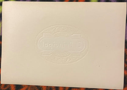 Cream-colored embossed cigar label with ornate oval border and "El Principal" text, displayed flat on colorful fabric