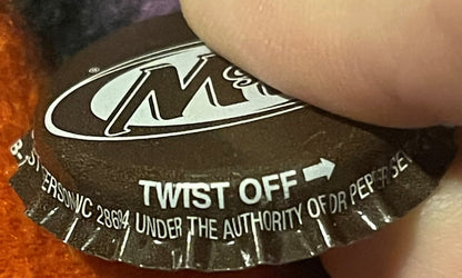Close-up of vintage A&W Root Beer twist-off bottle cap held by a finger, showing white logo and "Twist Off" text on black cro