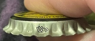 Edge of the Imitation Pineapple Soda cap held in the fingers: fluted metal skirt stamped with a small crown outline around the number 10 and a circled mark beside it