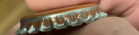 Vintage bottle cap held in hand showing corrugated metal edge and embossed text, close-up detail view