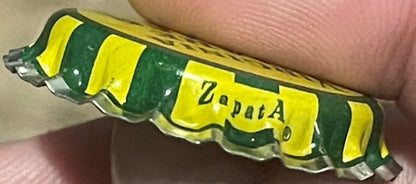 Vintage green and yellow striped bottle cap marked "Zapata" held in a person's hand for scale