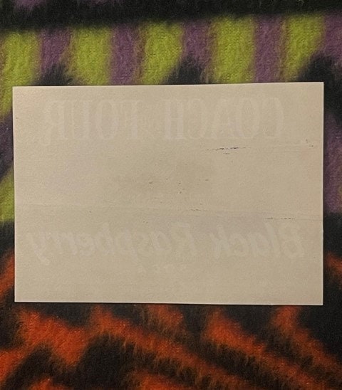 Blank cream-colored label or paper displayed on striped fabric background in shades of yellow, purple, and orange