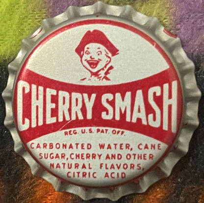 Vintage red and white Cherry Smash bottle cap with clown face logo and ingredients text, photographed flat on colorful surfac