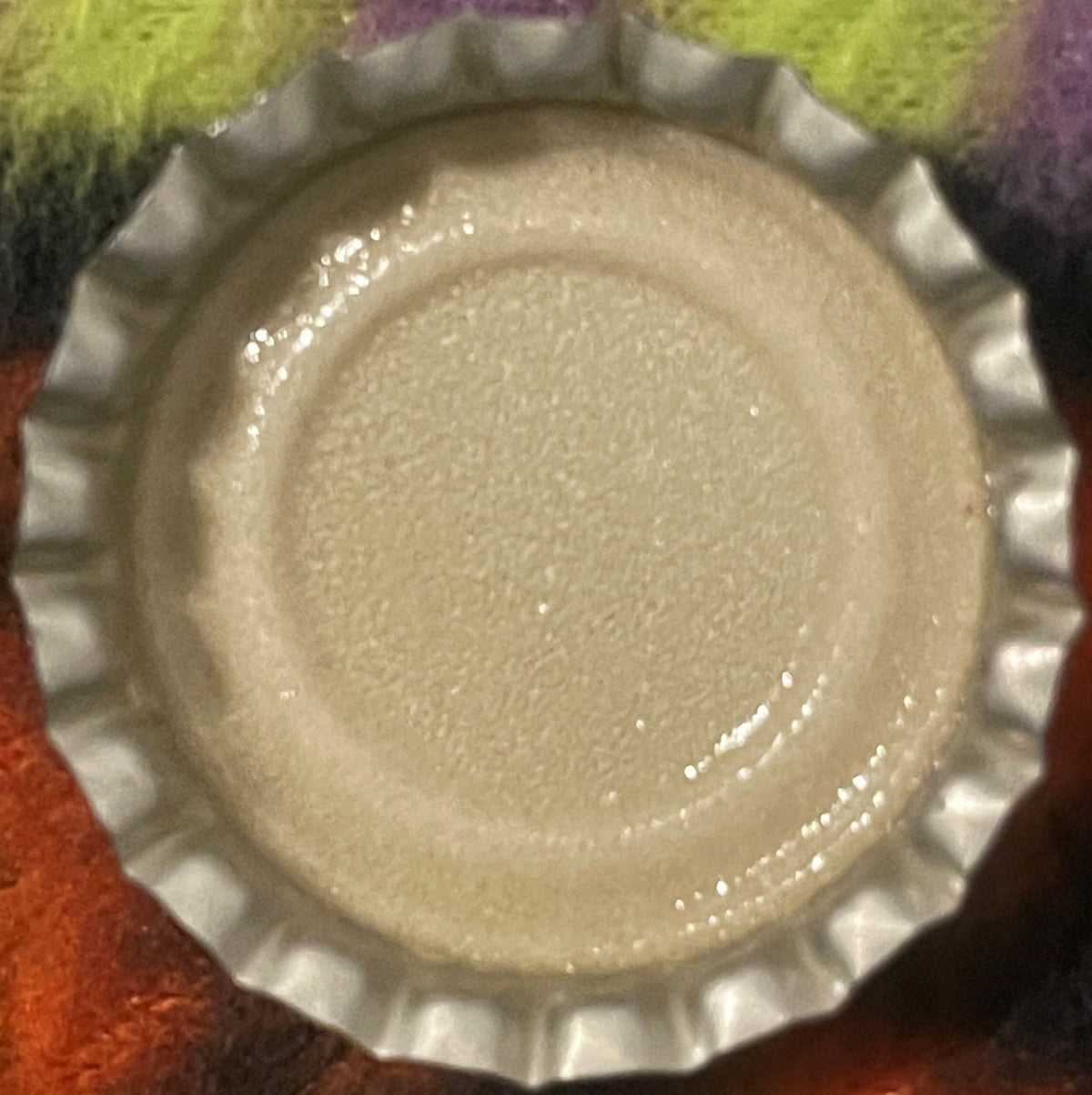 Vintage white metal bottle cap with ridged edges on colorful fabric background, top-down view