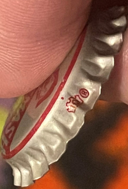 Vintage Cherry Smash bottle cap held against pink fabric for scale, showing embossed design and red text on white metal