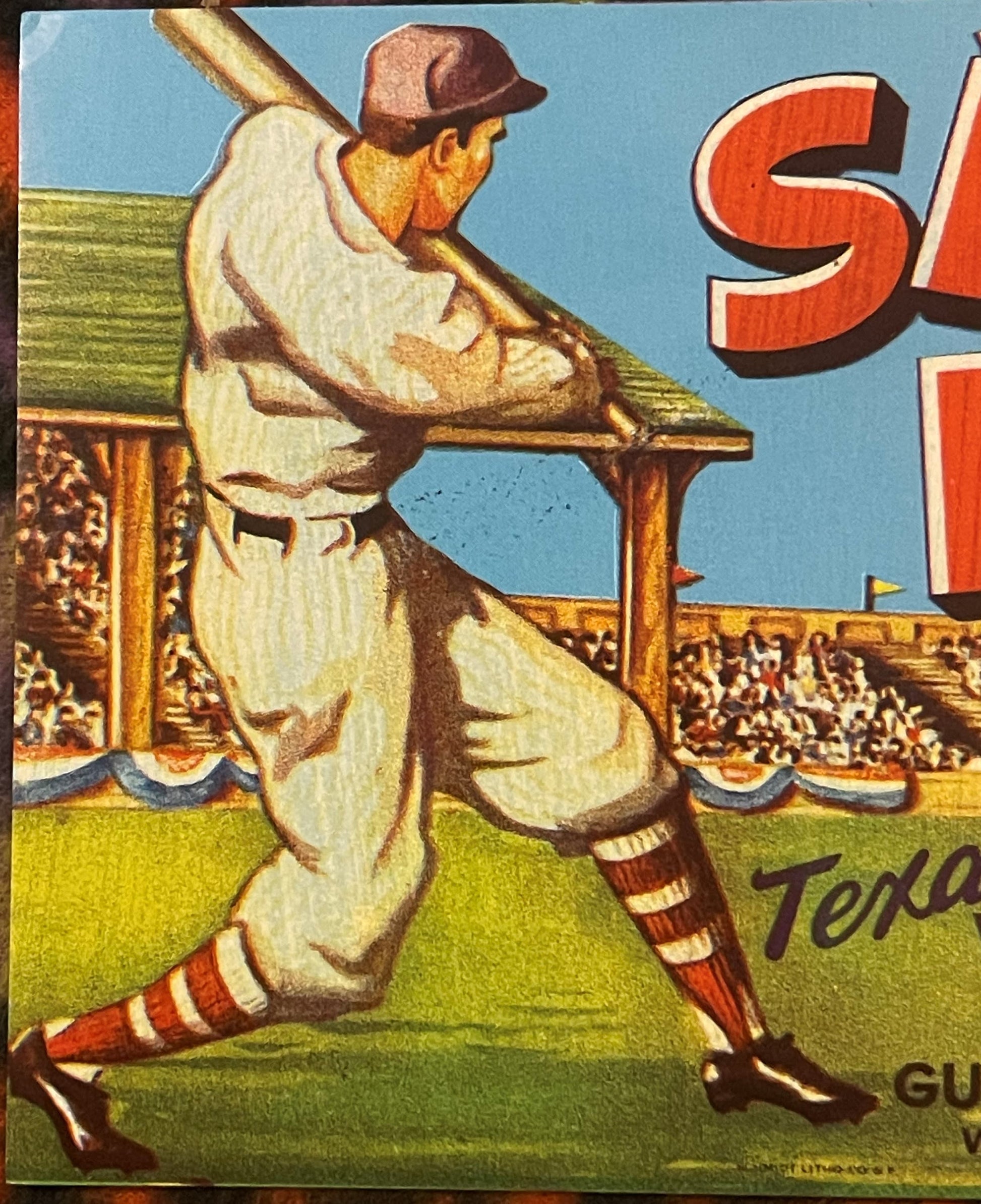 Vintage baseball crate label showing batter in white uniform mid-swing at stadium, red and white striped socks, brown cap, "S