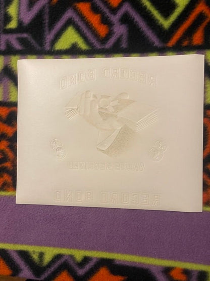 Back of the Record Bond cigar label: plain white paper with the embossed hand, coins and lettering pressed through in reverse, on a patterned blanket