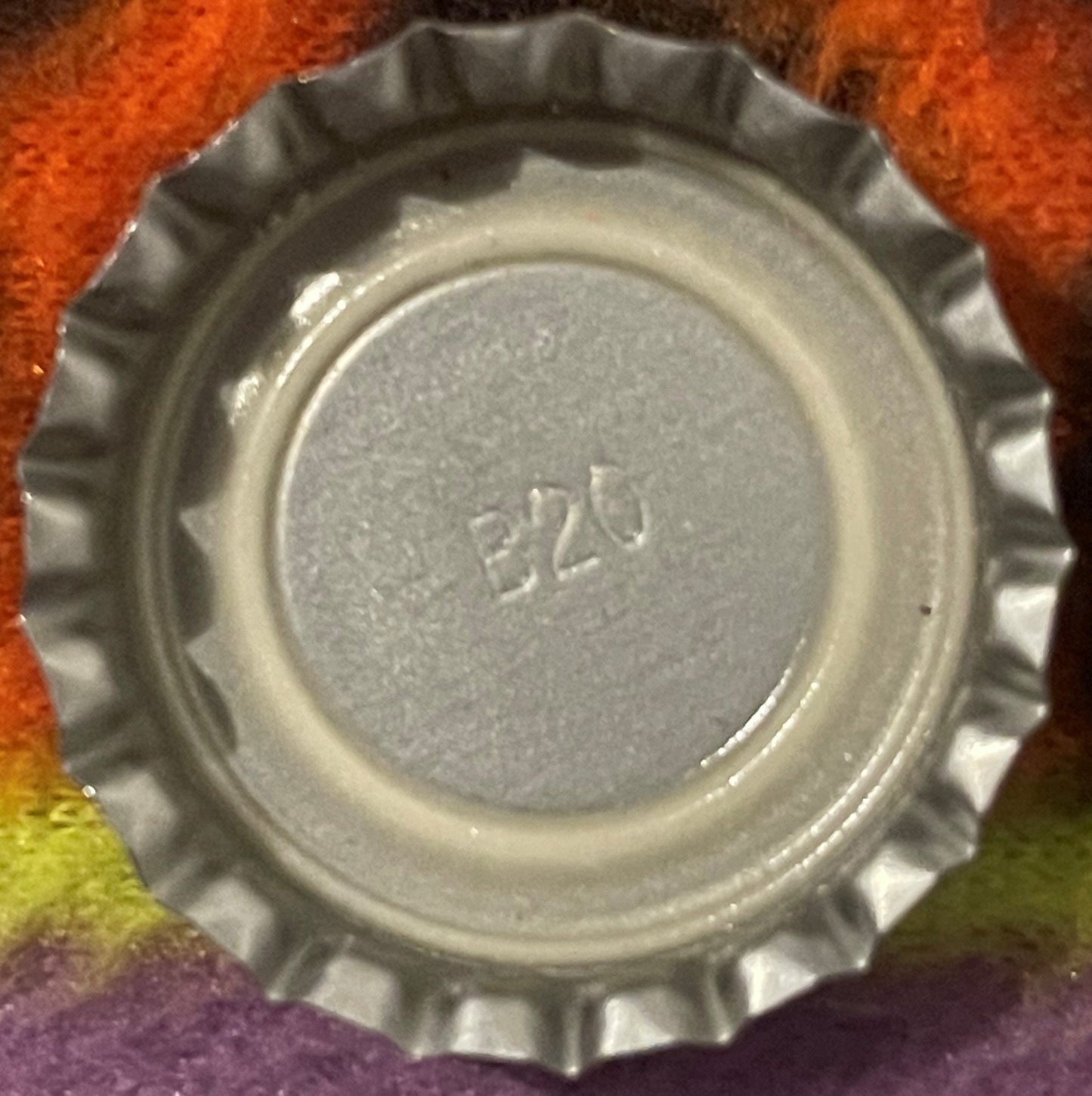 Close-up of a metal bottle cap with ridged edges and embossed numbers "8226" on gray center, photographed against colorful fa