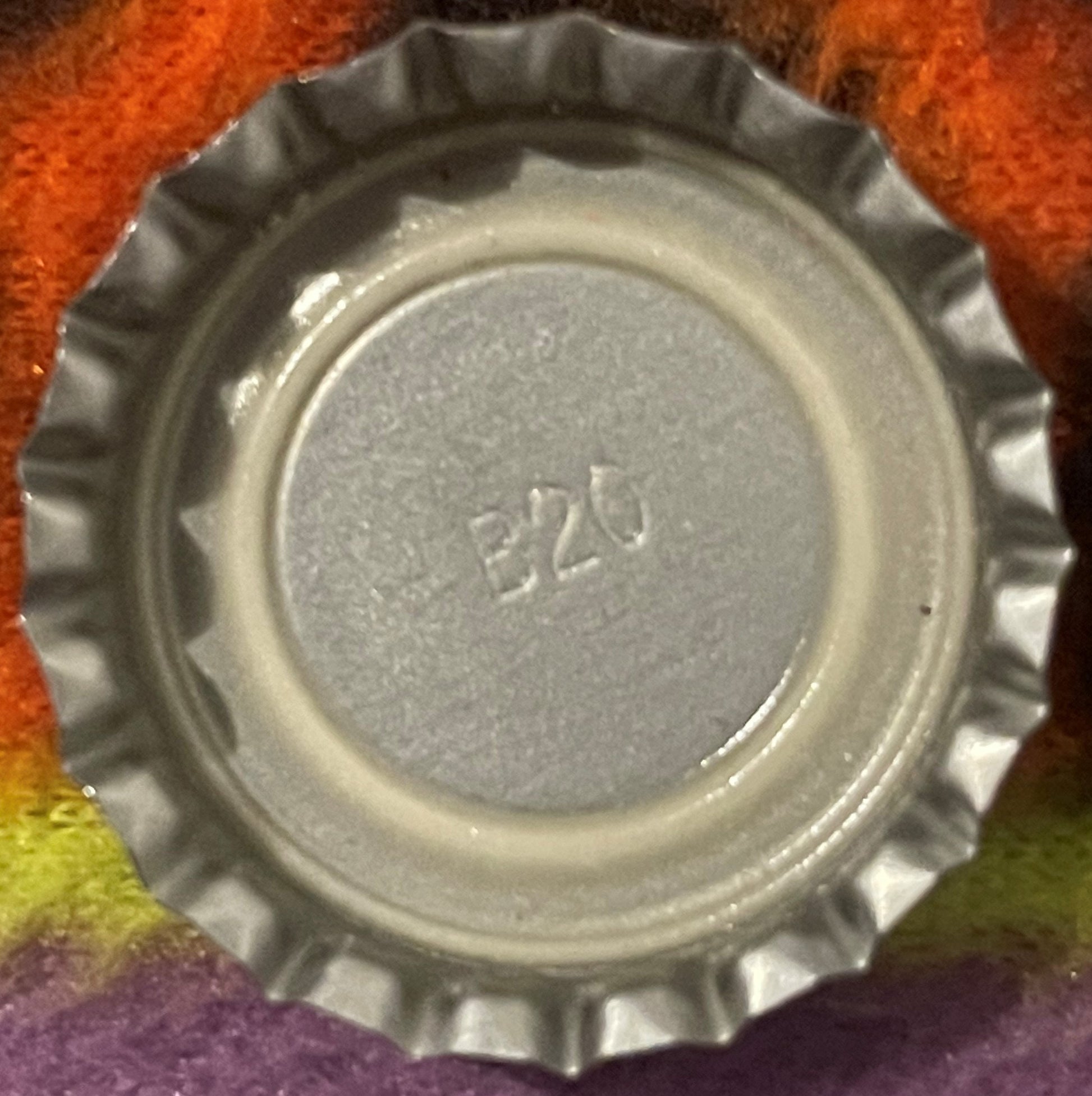 Close-up of a metal bottle cap with ridged edges and embossed numbers "8226" on gray center, photographed against colorful fa