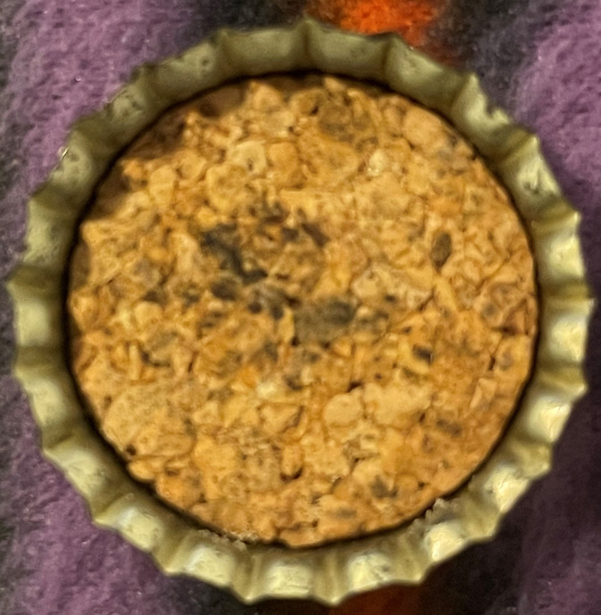 Antique King Bee Grape Soda cork-lined crown bottle cap viewed from above, showing tan cork lining and embossed bee logo on purple fabric background.
