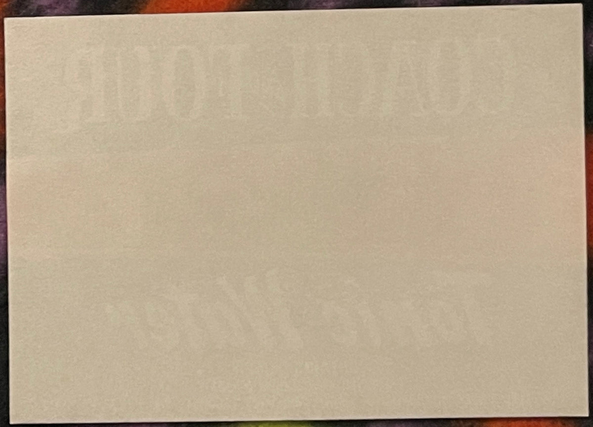 Blank cream-colored rectangular label or paper sample against a dark patterned background