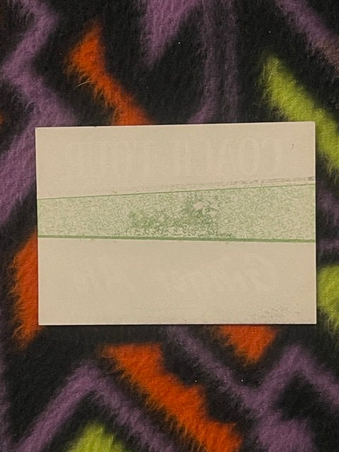 Vintage soda label with green band on cream paper, displayed on colorful striped fabric background for scale.