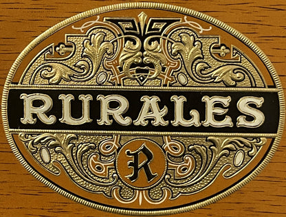 Embossed brass cigar label with ornate scrollwork reading "RURALES" on black band, mounted on wood grain background