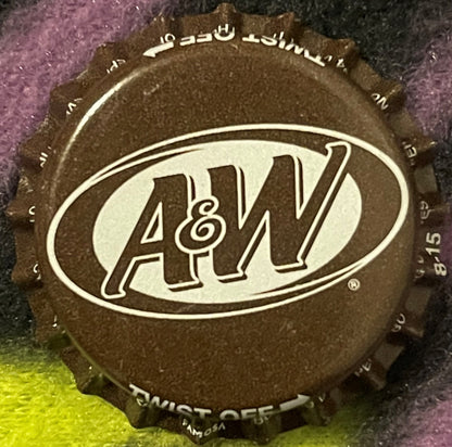 Close-up of brown A&W root beer bottle cap with cream-colored oval logo, ridged crown edge, and partial text visible on rim, 