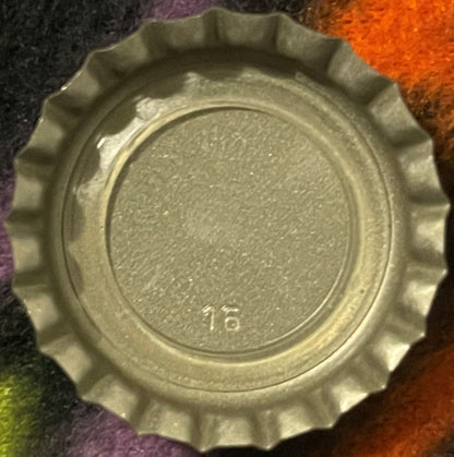 Cream-colored twist-off bottle cap with ridged edges and circular embossed design, showing partial text marking, photographed