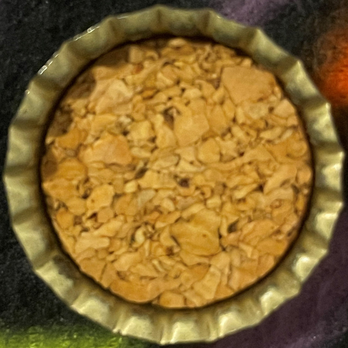 Overhead view of an antique bottle cap with a ridged metal rim and tan cork center, showing embossed texture typical of late 1930s–1940s soda bottle closures.