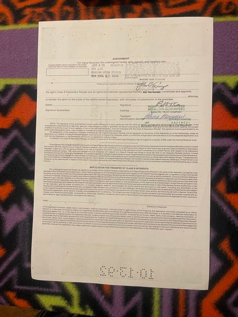 Vintage stock certificate on colorful patterned fabric background, showing handwritten signatures and printed text with orang