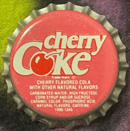Red and silver Cherry Coke bottle cap with cream-colored text showing ingredients and "1990-1345" marking, photographed flat 