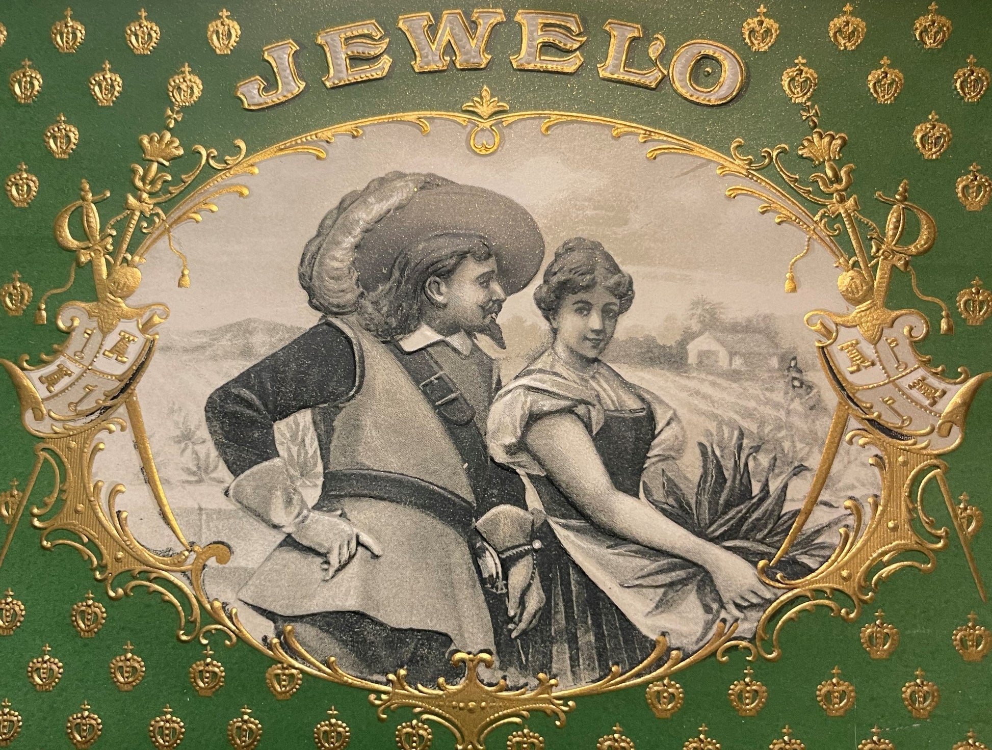 Antique Jewelo cigar label with gold embossed border, green background, and central engraving of a man and woman in period dr