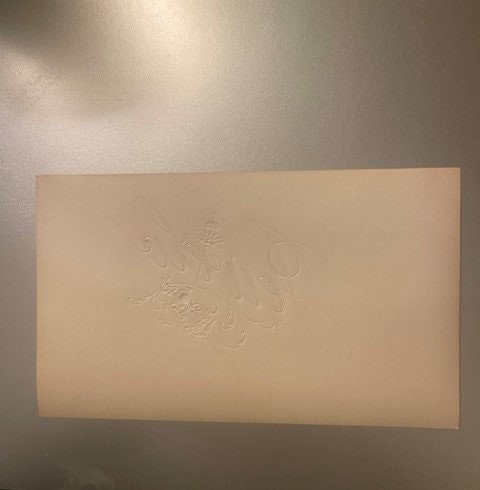 Cream-colored embossed cigar label with raised gold lettering on beige background, displayed flat against neutral wall